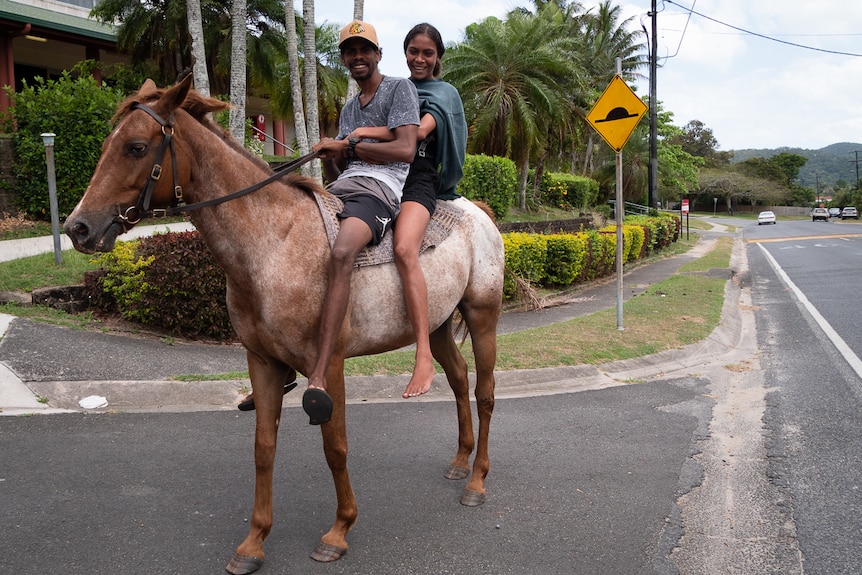 Two Aboriginal teens riding horse on community street