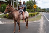 Two Aboriginal teens riding horse on community street