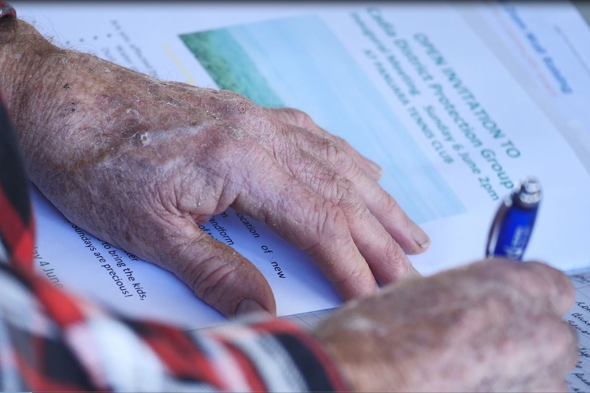 A hand poised over notebook, taking notes of a meeting