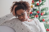 Woman looking sad next to Christmas tree
