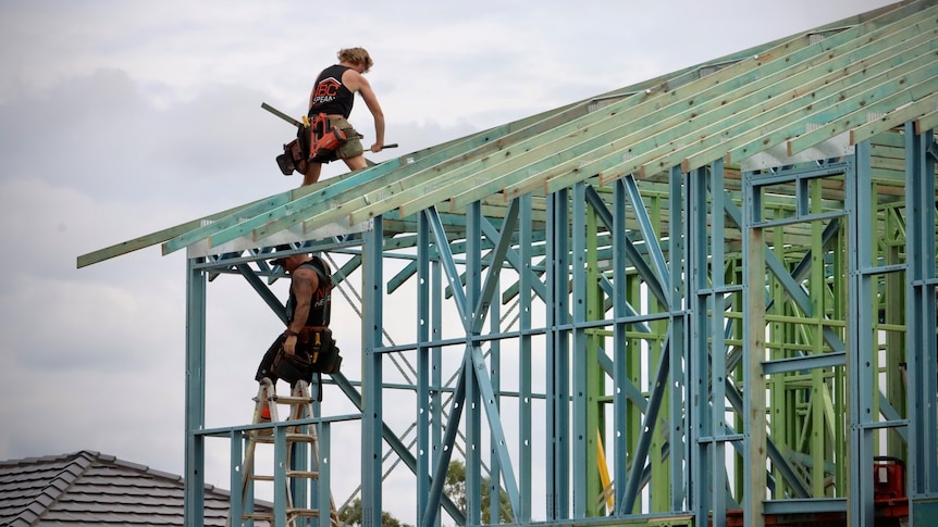 Tradies work on the roof frame of a new home under construction.