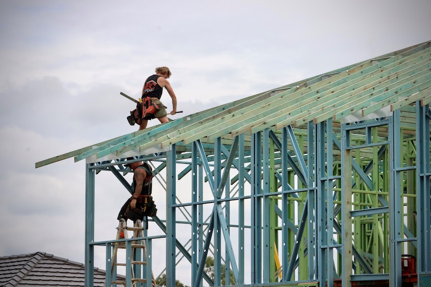 Tradies work on the roof frame of a new home under construction.
