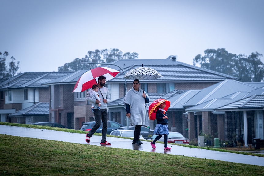 A young family walk down a footpath on a rainy day. Mum, Dad and little girl are all holding umbrellas