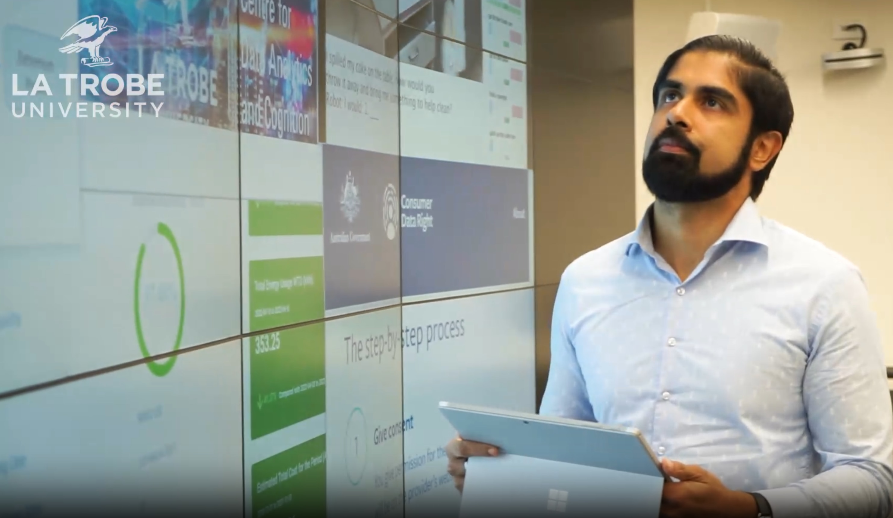 A man in a blue button shirt and a beard holding a tablet device.