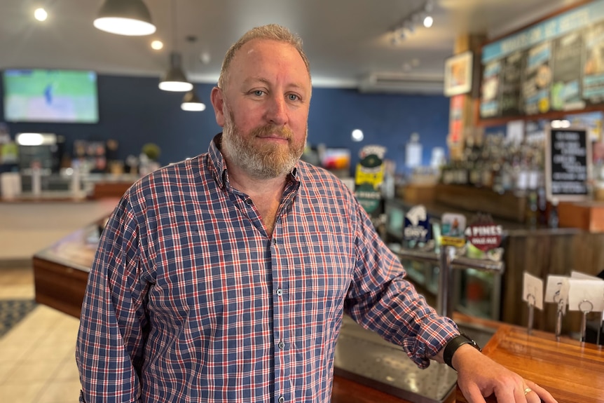 A male pub owner stands in front of a bar.