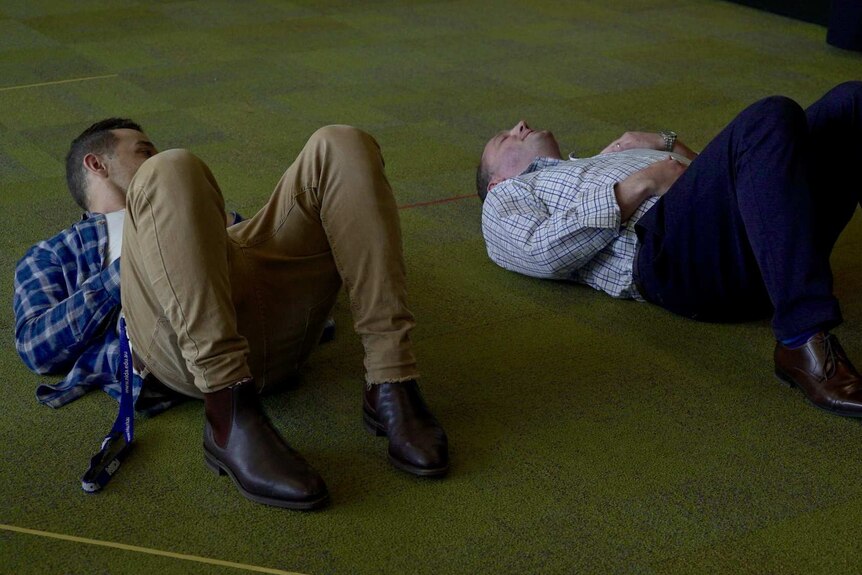 NIDA trainer Les Chantery lies next to ABC reporter David Taylor