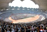 A wide image showing a large crowd in the stands and grounds of an open-roof stadium, many holding one hand in the air
