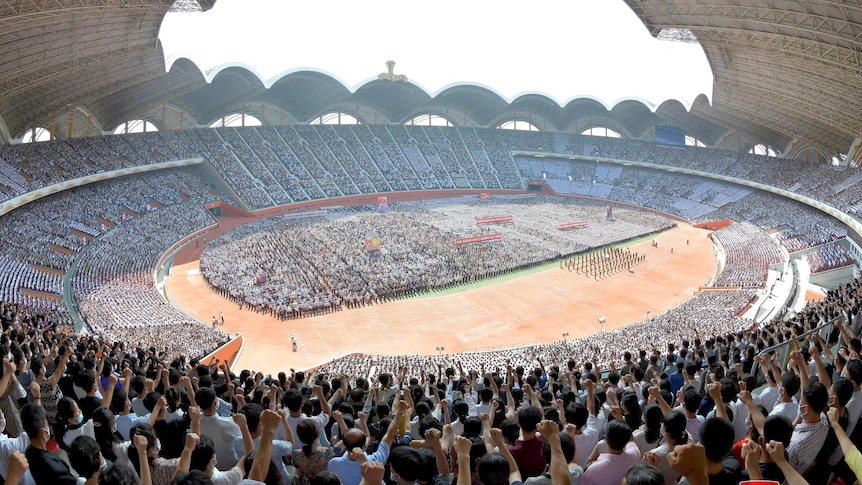 A wide image showing a large crowd in the stands and grounds of an open-roof stadium, many holding one hand in the air