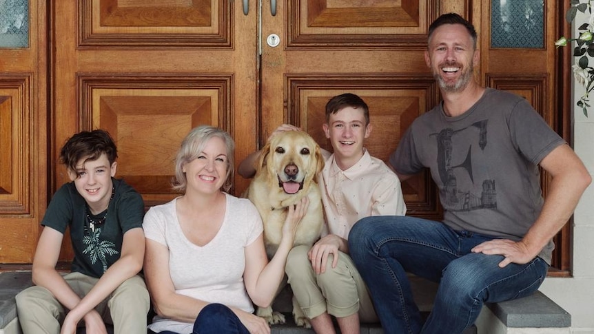 Couple seated on the stairs with their two sons and a dog.