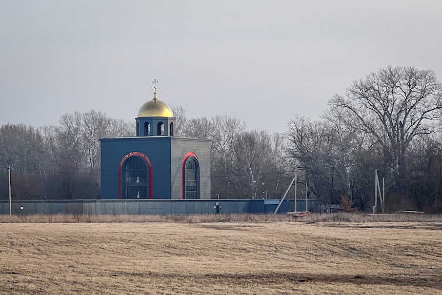 A black red and gold chapel building is seen on the edge of a dirt hill.
