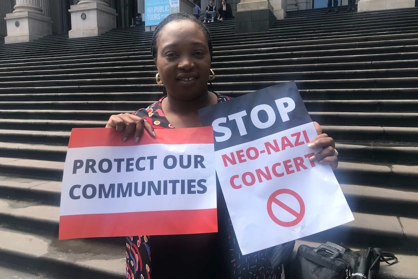 Abiola Ajetomobi holds two signs calling for the protection of communities and to stop a neo-Nazi concert.