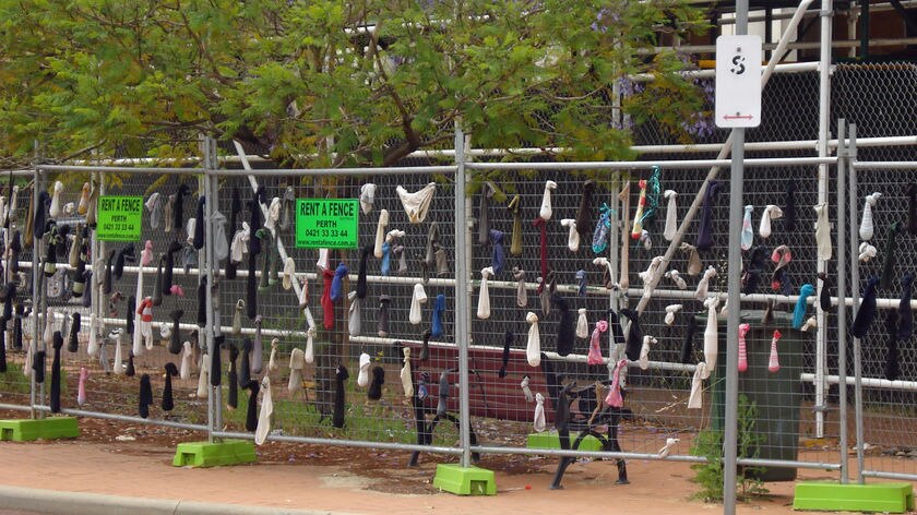 Hundreds of socks have been added to the fencing to show locals' displeasure at the delay in rebuilding