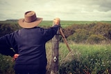 A man leaning on a fencepost looking over a rural vista.