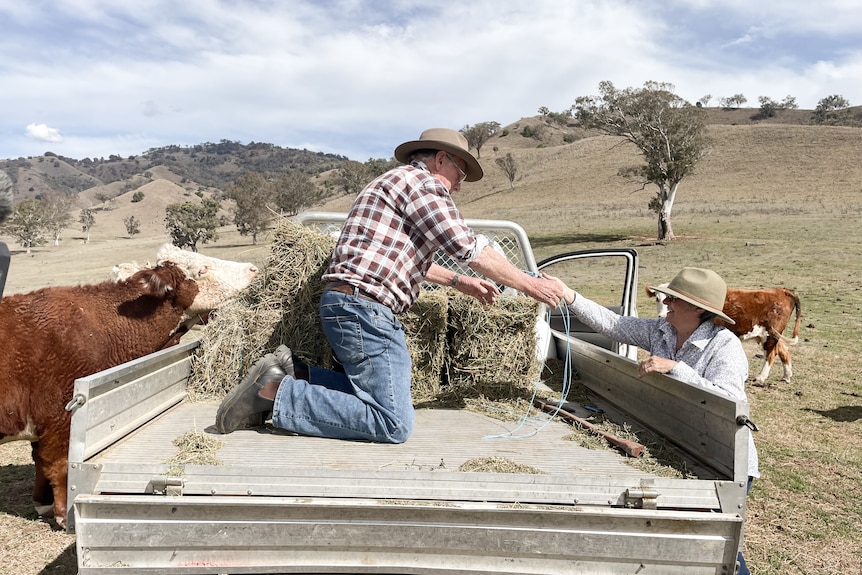 A man and woman unload bales of hay from a truck