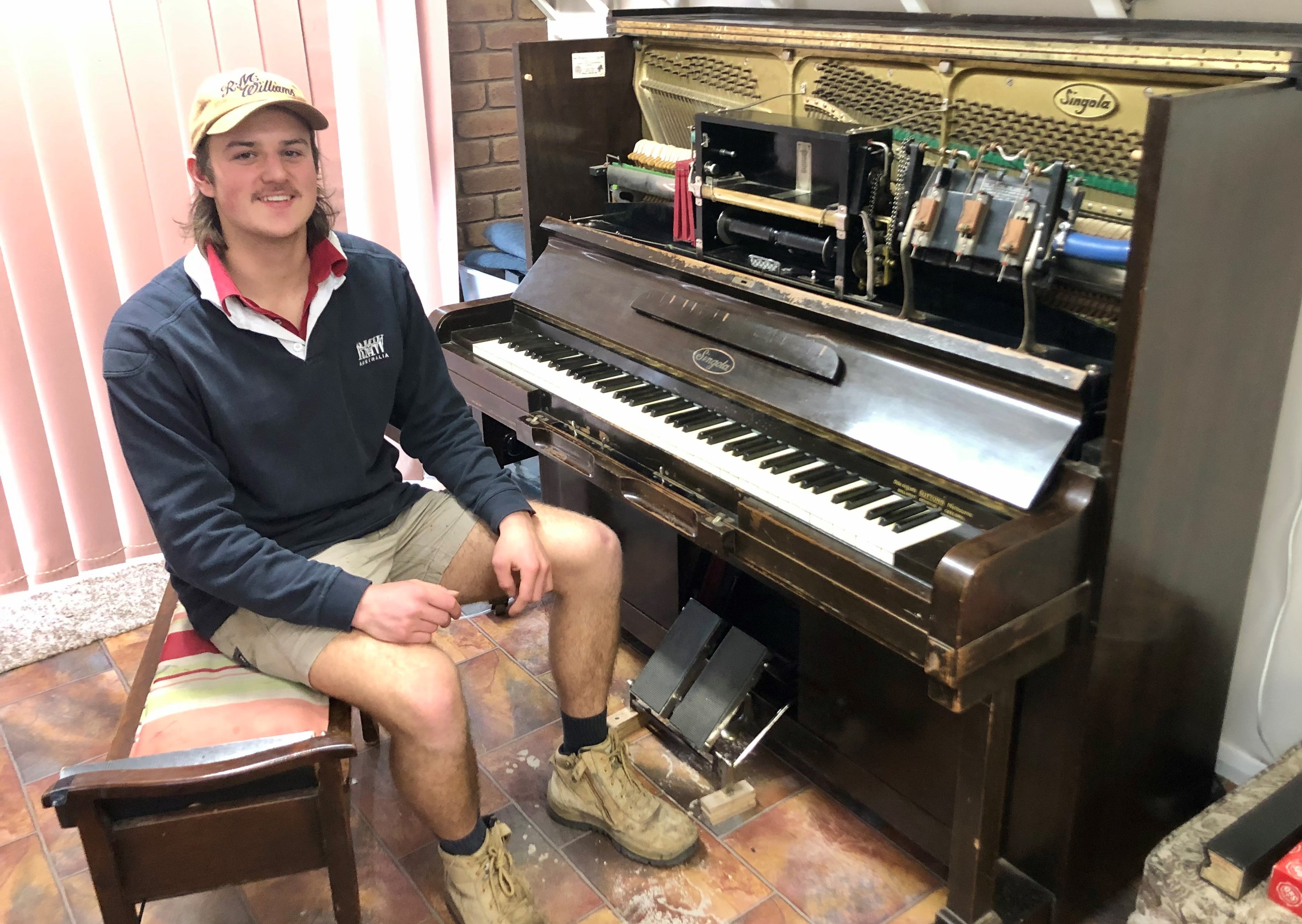 A man in sits in front of an old wooden player-piano 