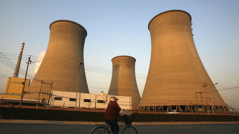 A woman rides her bicycle past a coal power station in Beijing.
