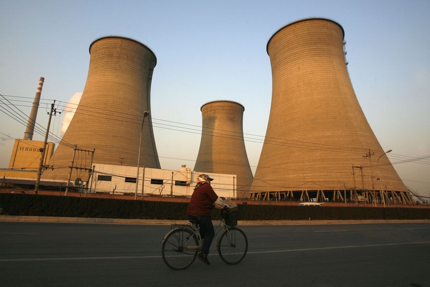 A woman rides her bicycle past a coal power station in Beijing.