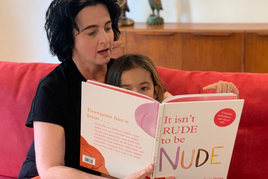 A woman sits on a couch reading to a young girl for a story on teaching positive body image