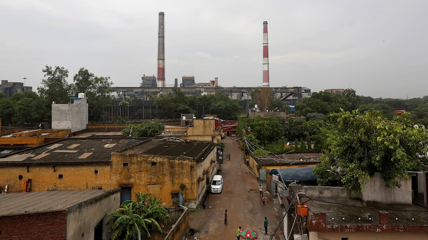 Two red and white chimneys from a factory dot the skyline of a gritty Asian town on a cloudy day