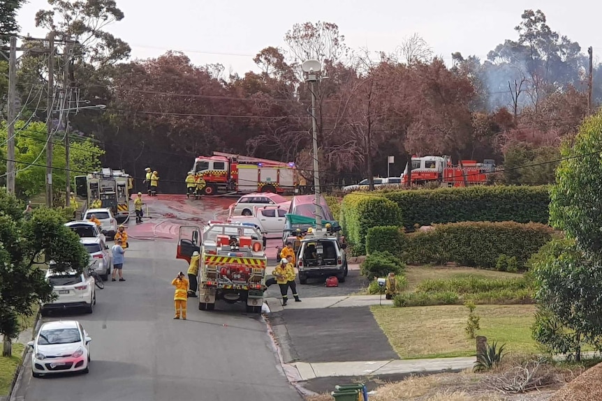 Firefighters on a suburban street with smoke in the background.