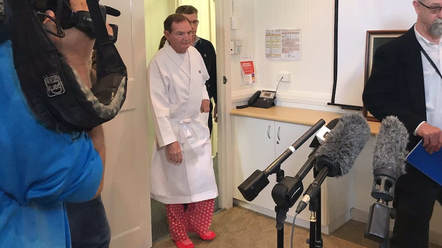 Paul Pisasale in a hospital gown enters a room full of journalists