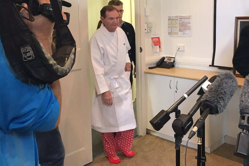 Paul Pisasale in a hospital gown enters a room full of journalists