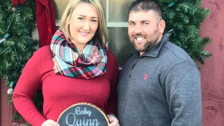 Kevin Quinn and his wife pose with a sign announcing they were expecting a child.