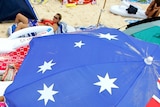 Beachgoers relax under an Australian flag beach umbrella