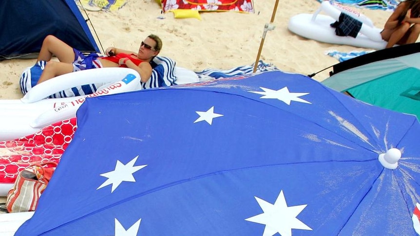 Beachgoers relax under an Australian flag beach umbrella