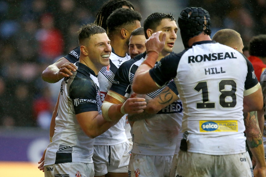 English rugby league players smile and hug in celebration after a try during a big game.