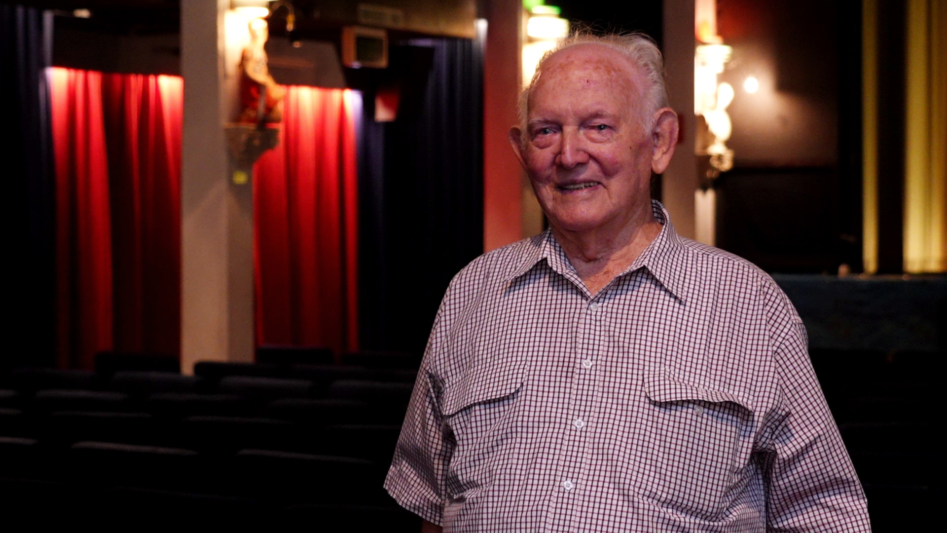 An old man smiles inside a old-fashioned movie theatre