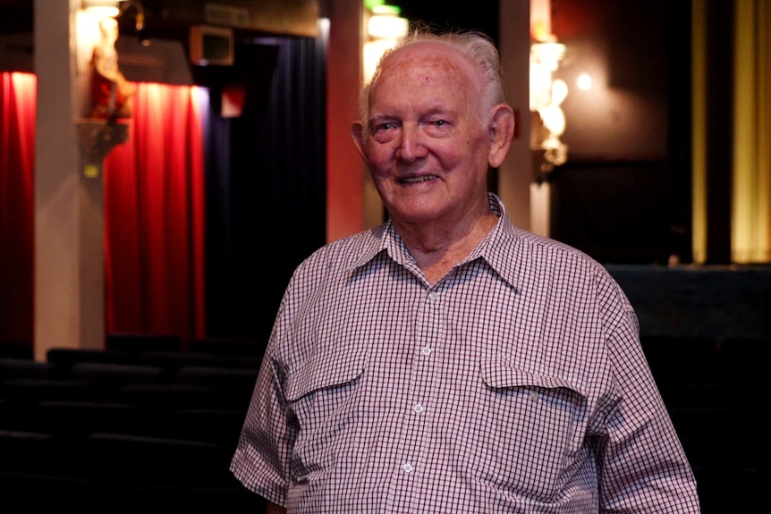 An old man smiles inside a old-fashioned movie theatre