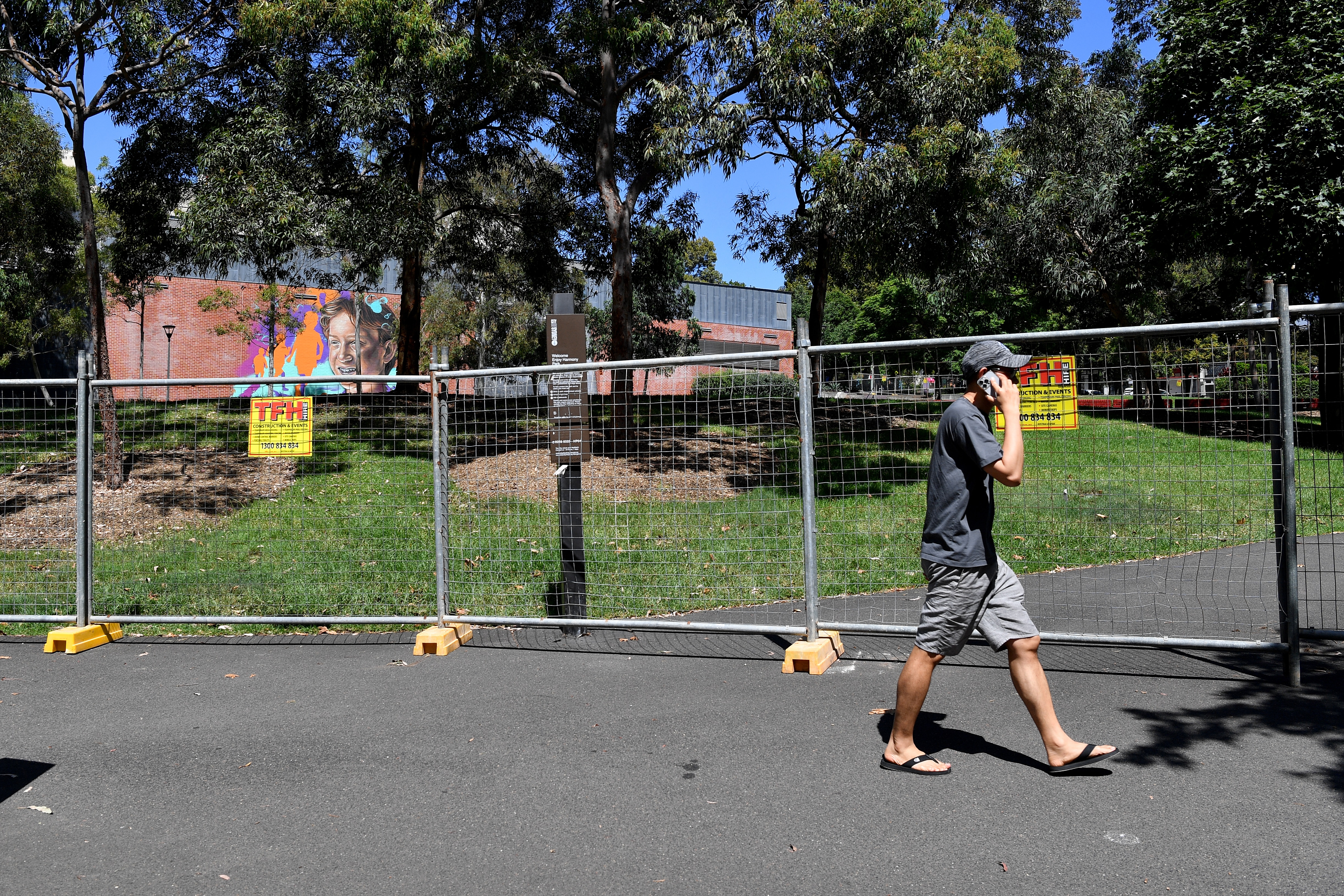 A man on the phone walking past a fenced park 