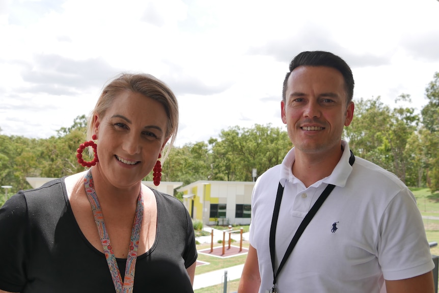 A woman and a man are smiling, there are buildings in the background