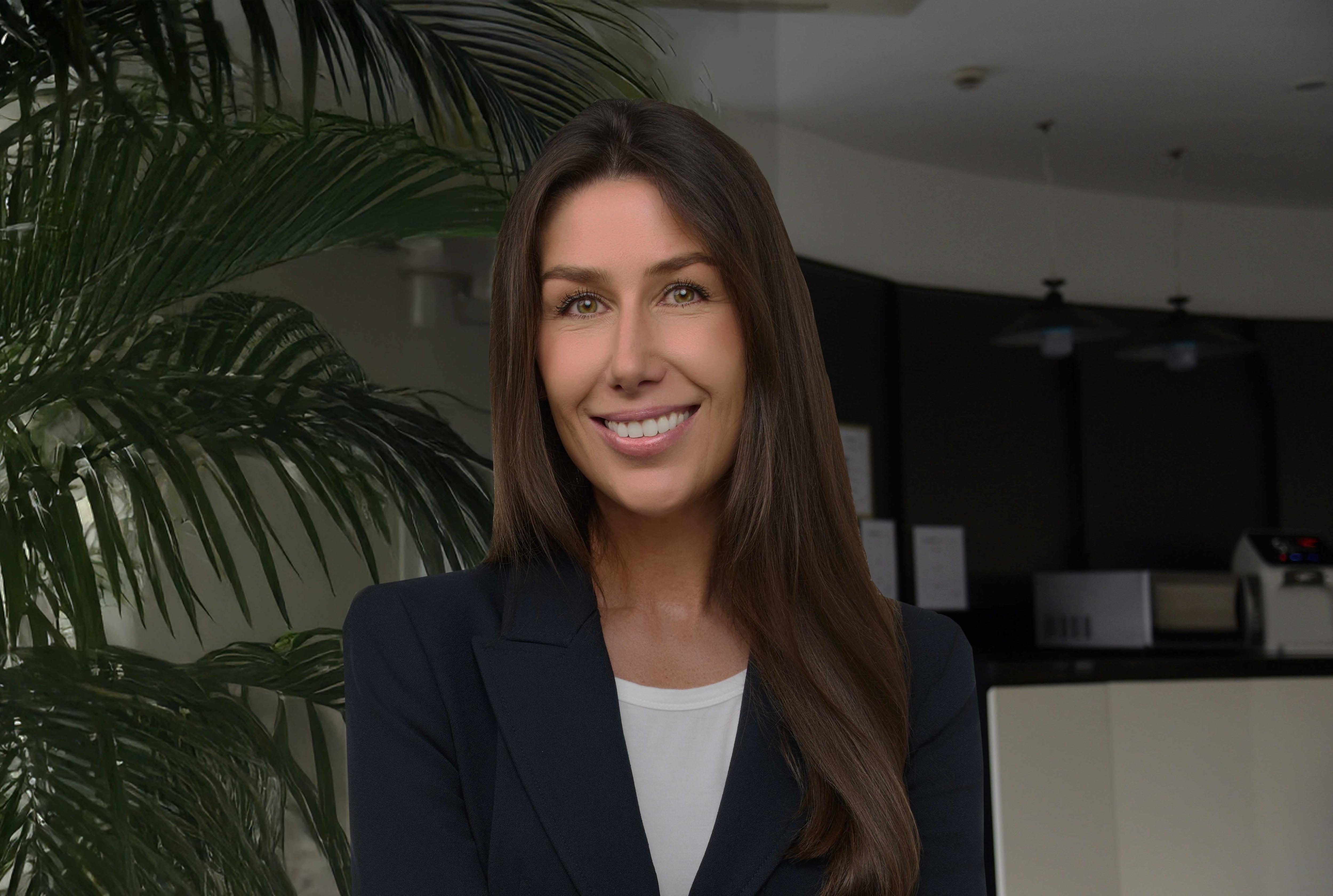A woman wearing a blue blazer smiles in front of a palm tree.