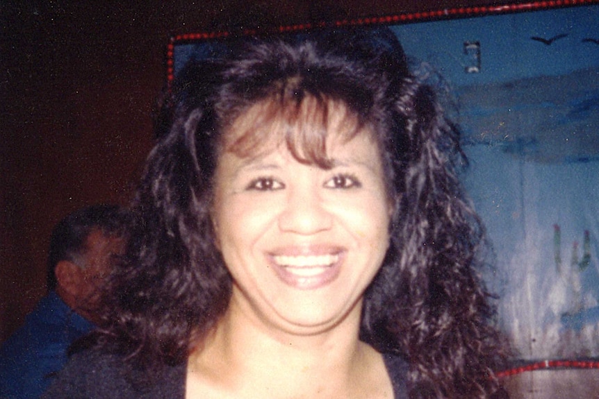 A young woman with curly 1980s-style hair smiles at the camera.
