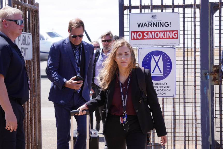 A woman and two men at an airport tarmac.