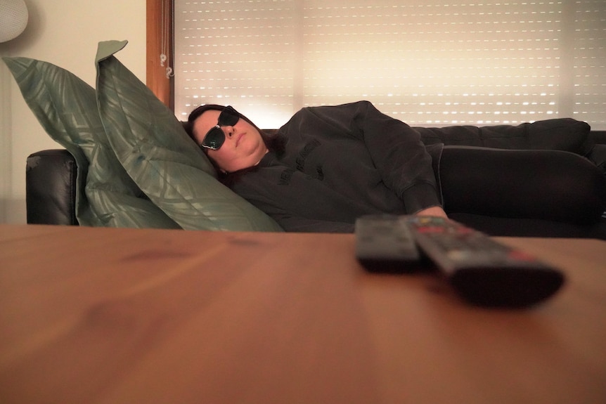 A woman lies on her sofa while wearing sunglasses and black clothes, with a coffee table in the foreground
