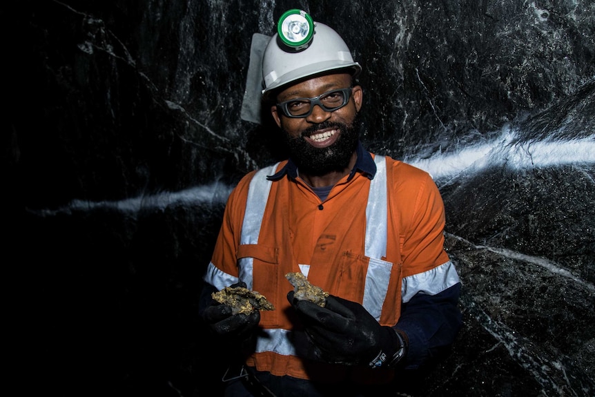 A mine worker in high-vis clothing holding gold specimens in an underground gold mine.