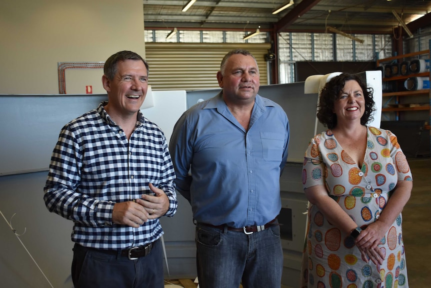 Two men and a women standing together inside a shed.