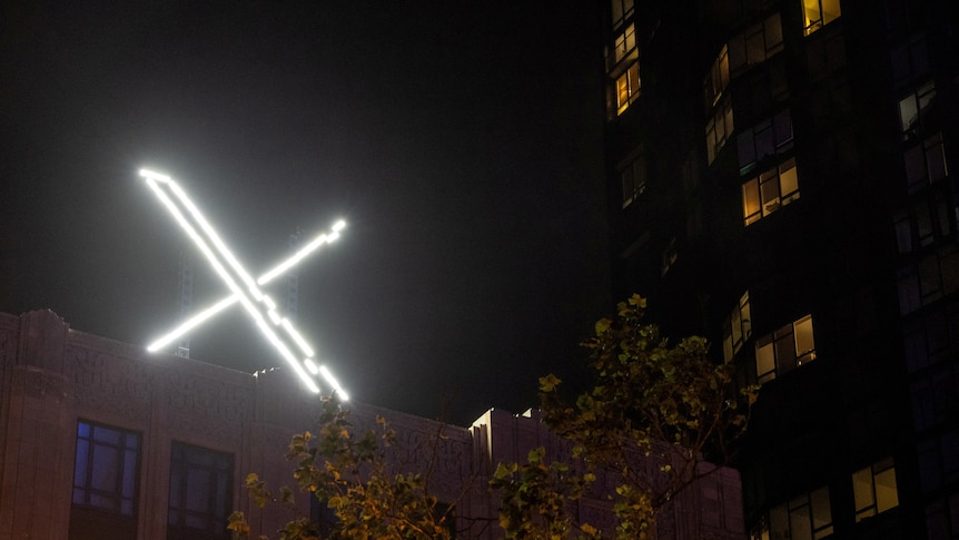 A LED light spelling the letter X is seen on top of an office building at night 