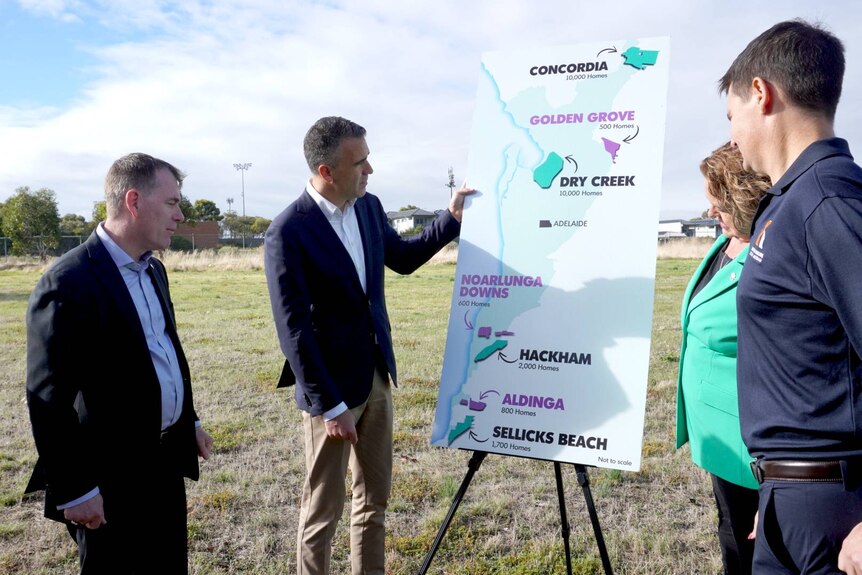 Four people stand around a map showing land marked for development.