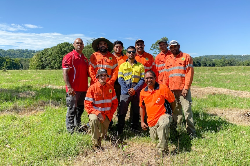 A group of men wearing hi-vis stand together for a photo, with two kneeling in front.