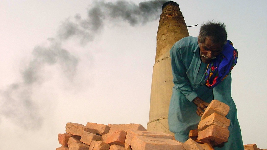 A Pakistani bonded labourer works on a brick kiln near Sukkur in Pakistan with smoke stack behind