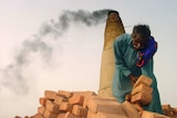 A Pakistani bonded labourer works on a brick kiln near Sukkur in Pakistan with smoke stack behind