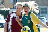 Two women run next to each other looking at a bouncing soccer ball that is in front of them at waist height.