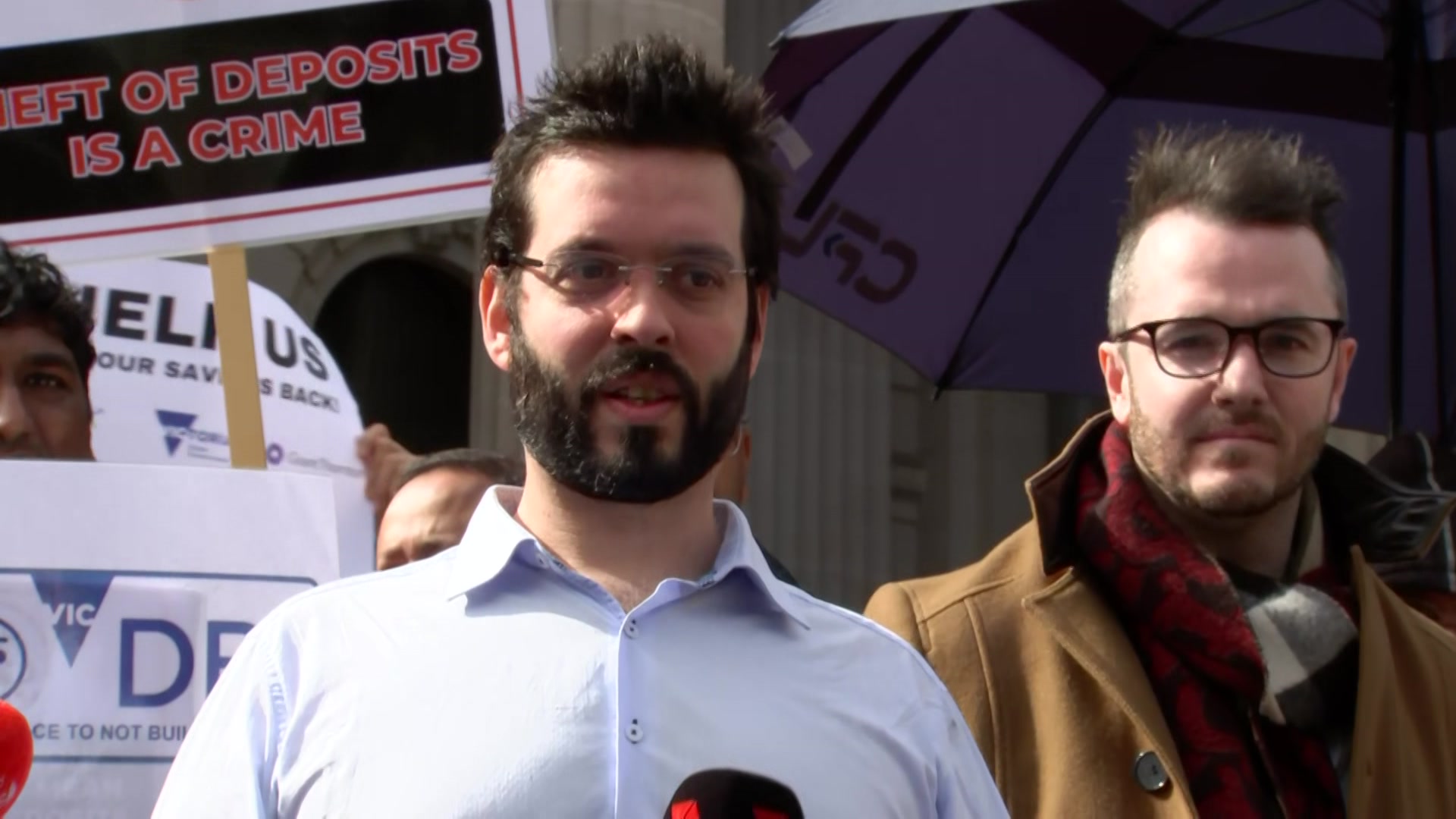 A man wearing a blue shirt  and glasses speaks into a microphone.