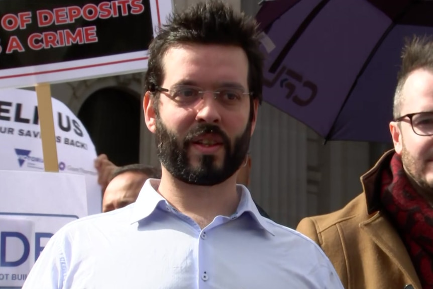 A man wearing a blue shirt  and glasses speaks into a microphone.