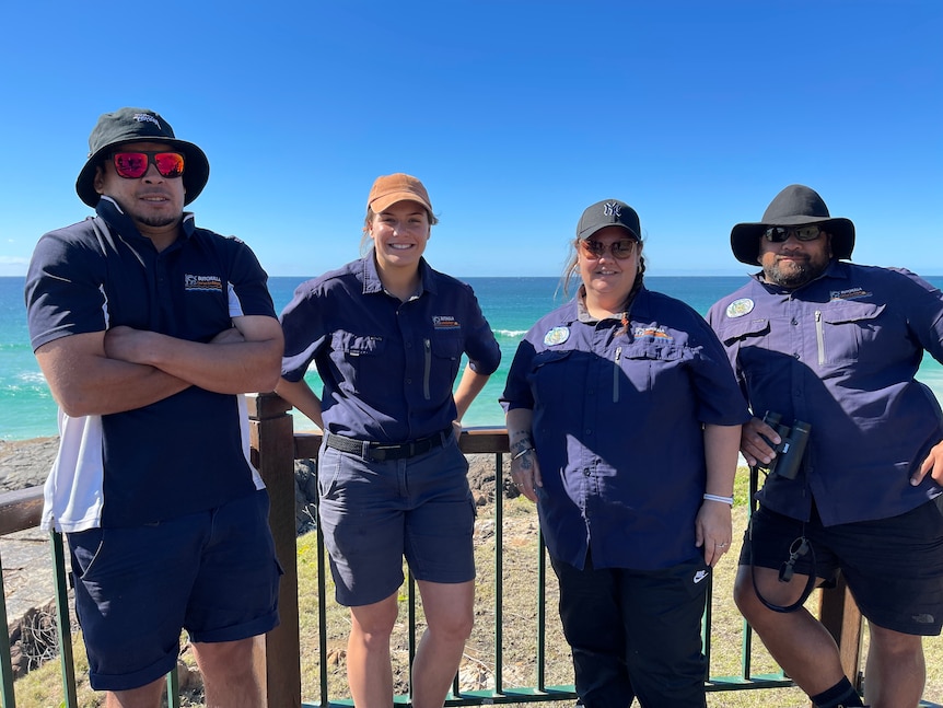 two men and two woman wearing ranger uniforms are standing and smiling with the ocean in the background