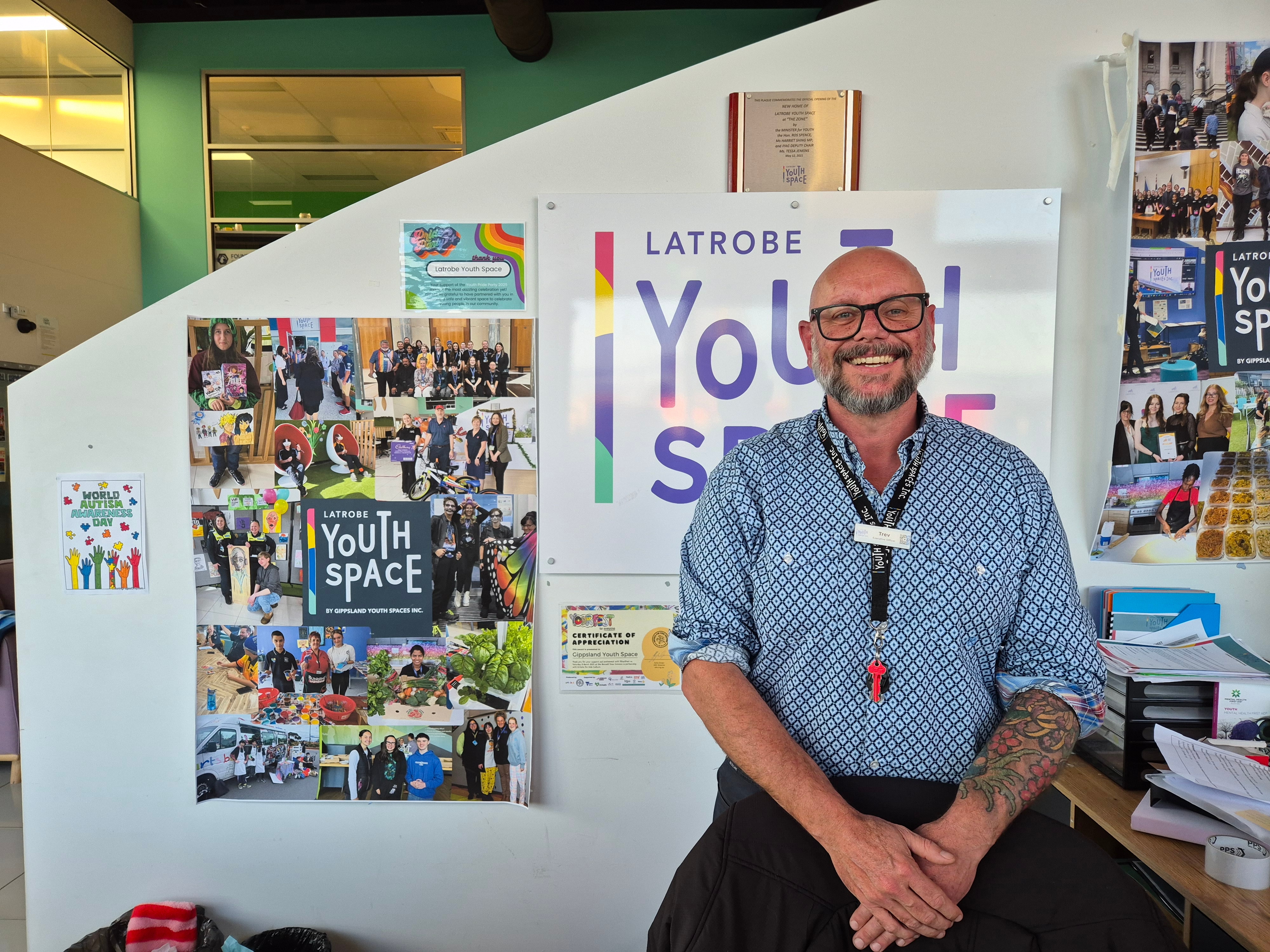 A middle aged man in a business shirt stands in front of Youth Space signs and photos, smiling